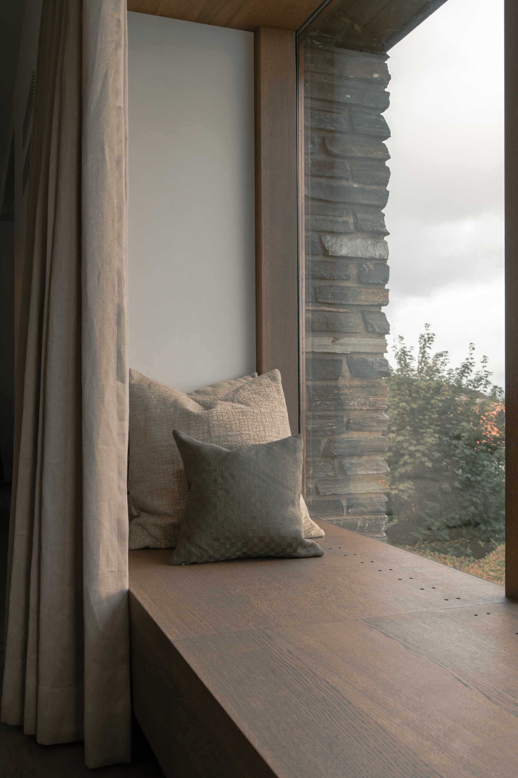 Cozy window seat with a wooden ledge, neutral cushions and linen curtains