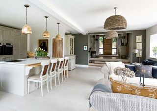 kitchen open plan with view of white wood edged island with painted wooden chairs and sofa and armchairs pale green cabinets and white tiled floor