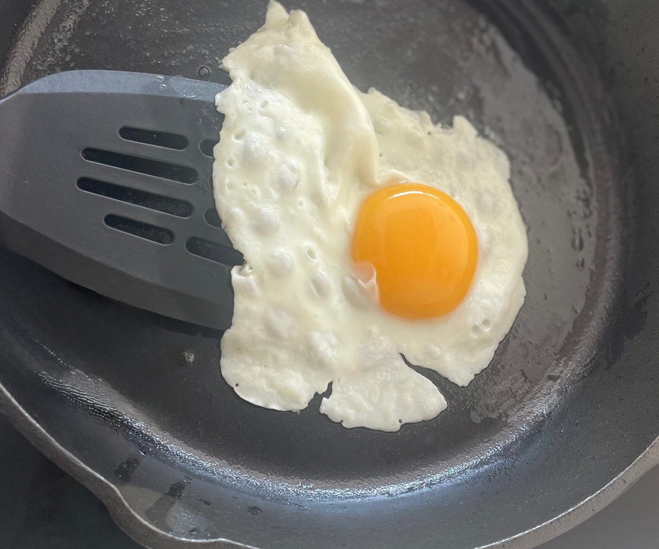 A black spatula lifting the edges of an fried egg in a black skillet
