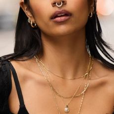 A woman wearing a septum piercing, earring stacks, and layered gold necklaces all from Banter jewelers.