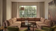 Image of a neutral living room with a window on the back wall and curtains that are pulled back. There is a large, U-shaped peach sofa, two olive accent chairs, and a wooden coffee table in the room.