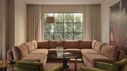 Image of a neutral living room with a window on the back wall and curtains that are pulled back. There is a large, U-shaped peach sofa, two olive accent chairs, and a wooden coffee table in the room.