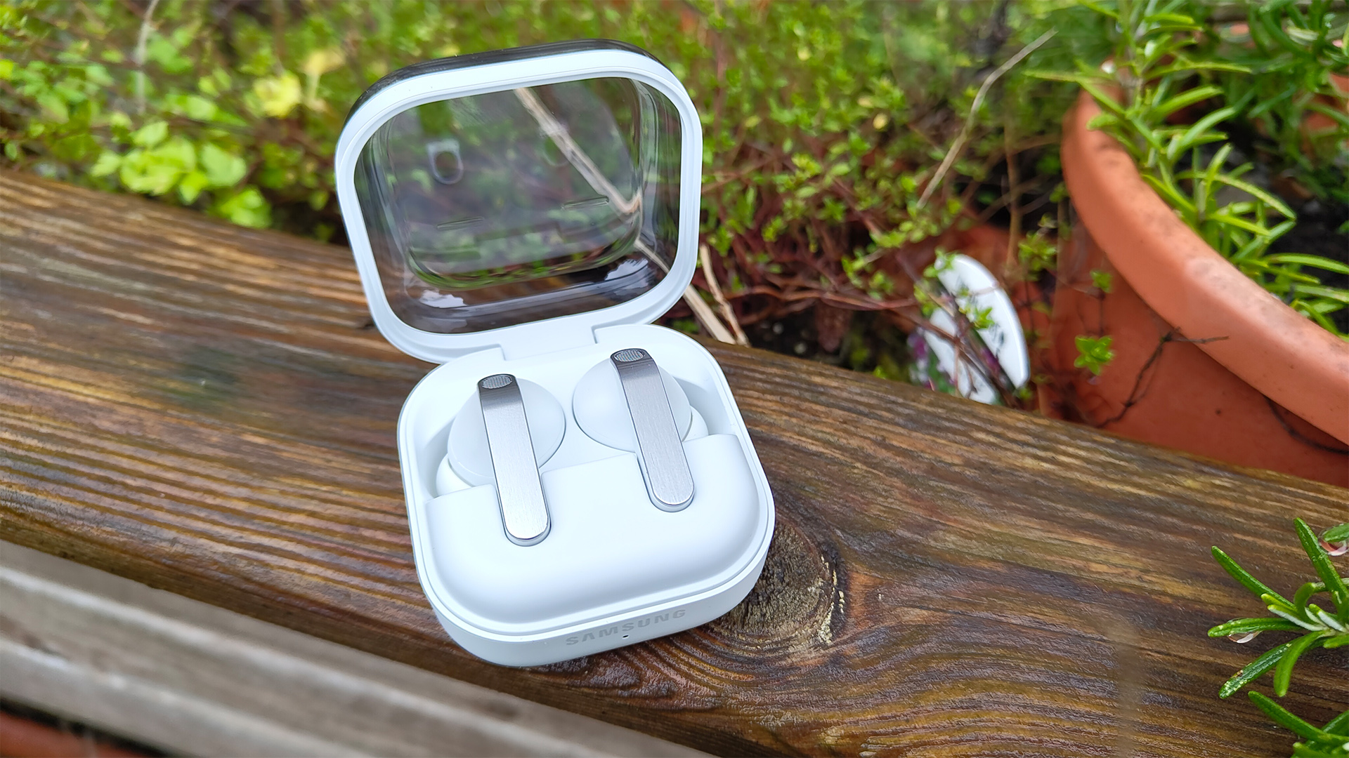 Samsung Galaxy Buds 4 Pro wireless earbuds in open case on wooden garden furniture with plants behind