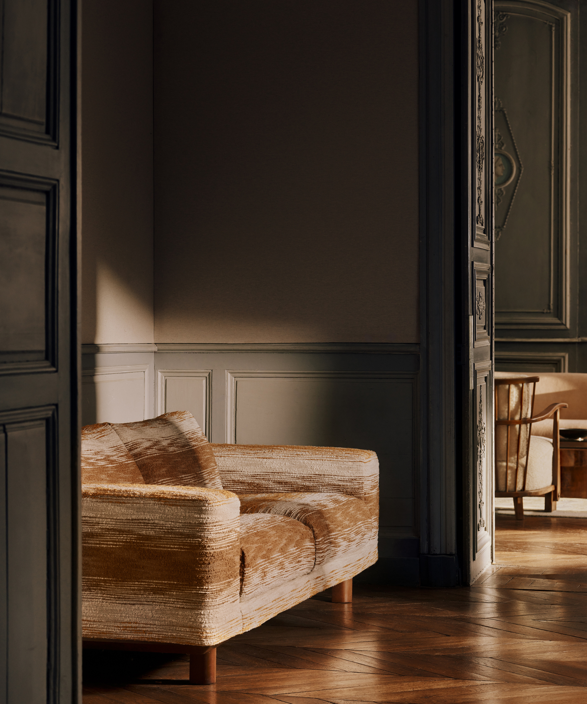 Stripey caramel-and-beige boucle upholstered sofa styled in a traditional nook with wooden herringbone floors and muted moss molding.