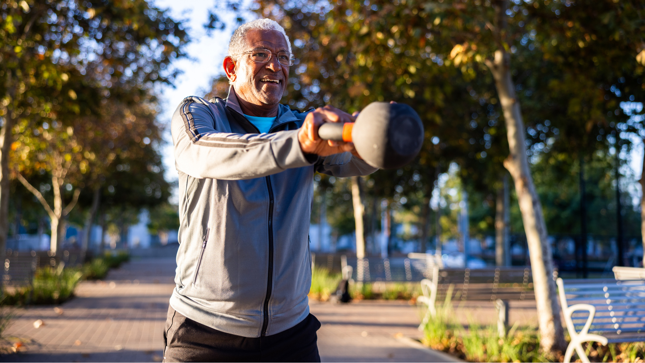 Senior man performing the kettlebell swing exercise in a park