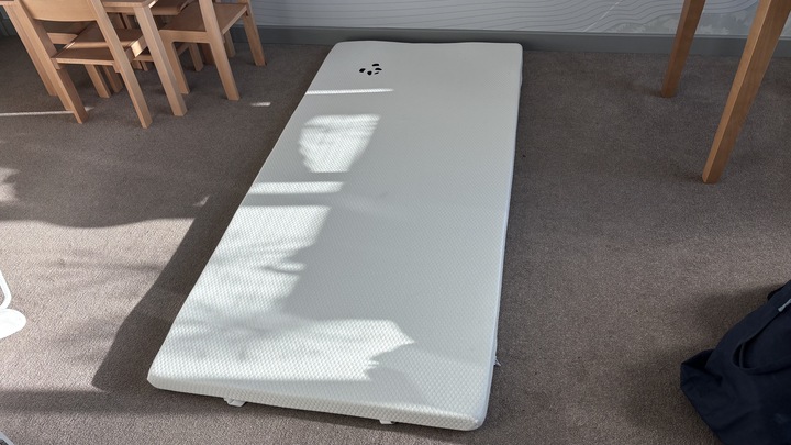 The Panda London Bamboo Mattress Topper placed on a brightly-lit carpeted floor.