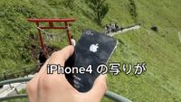 An iPhone 4 being held by photographer Takanobu Sasaki, in front of a green hill with a traditional red Japanese gate