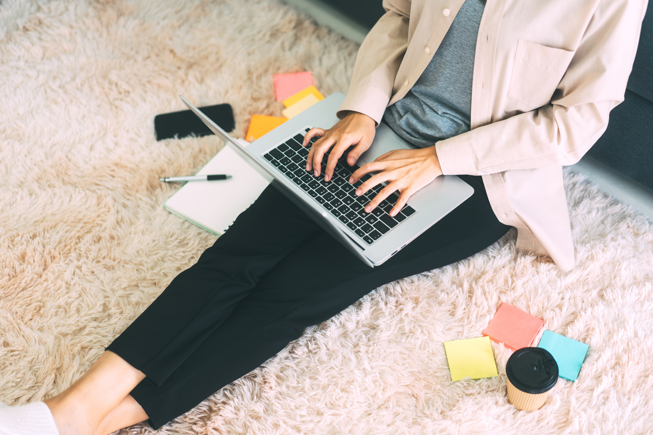Woman hand typing laptop computer keyboard sitting on carpet.