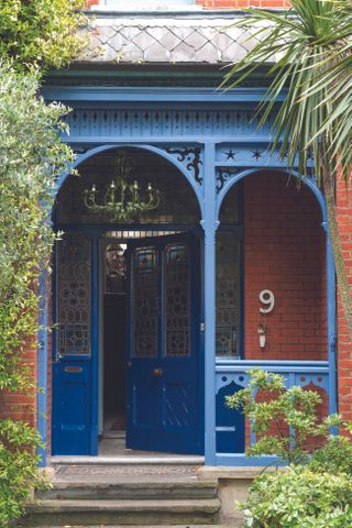 A blue recessed front door behind a blue archway and veranda. The house is white with creepers on each side of the archway