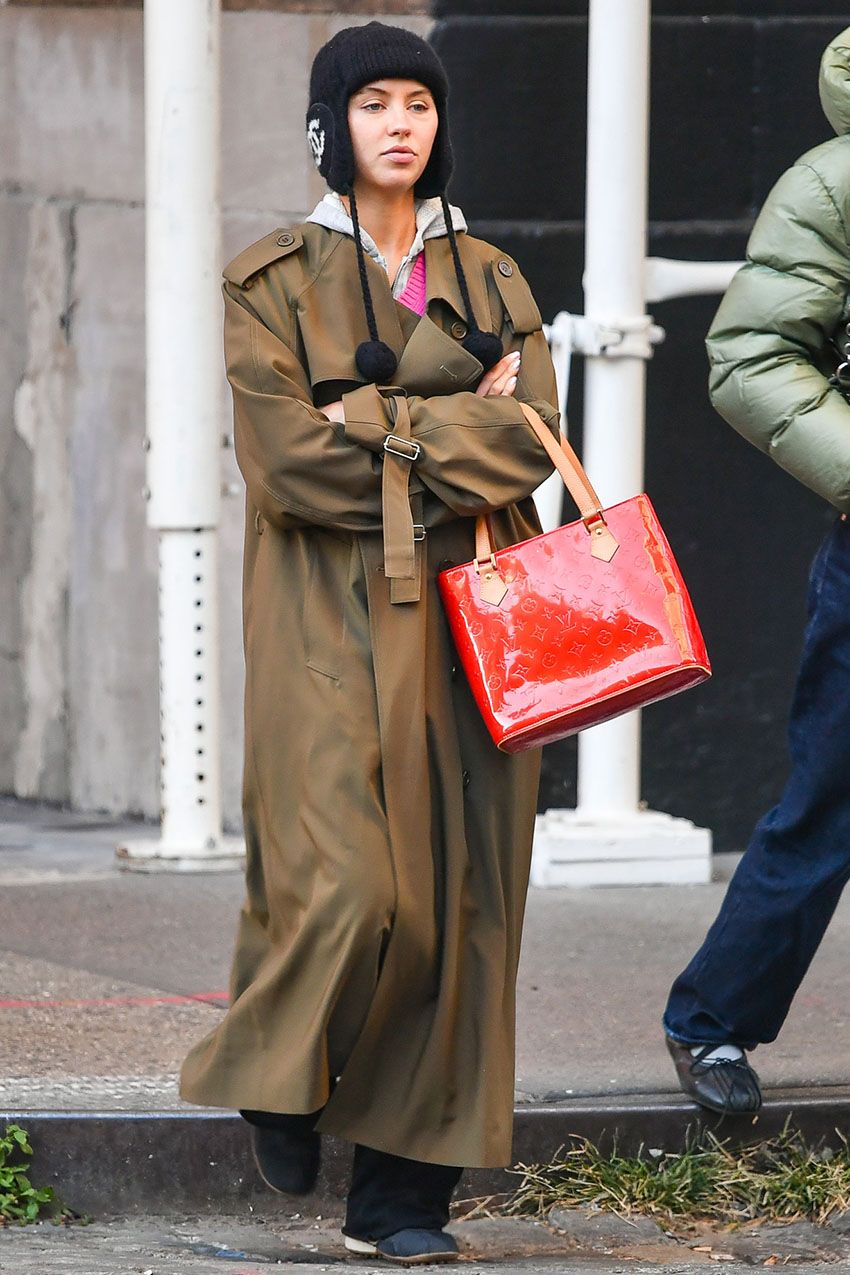 Iris Law wearing a black hat, trench coat, and red handbag