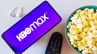 HBO Max app on a phone next to a bowl of popcorn, headphones and remote control