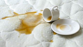 Image shows a cup of black tea spilled on a white mattress