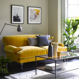Velvet mustard sofa with accent cushions in living room, coffee table, and hanging artwork
