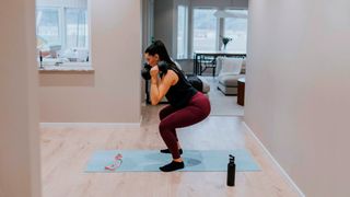 Woman performs dumbbell front squat at home