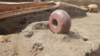 A red colored bead is shown beside a skeleton in a burial site.