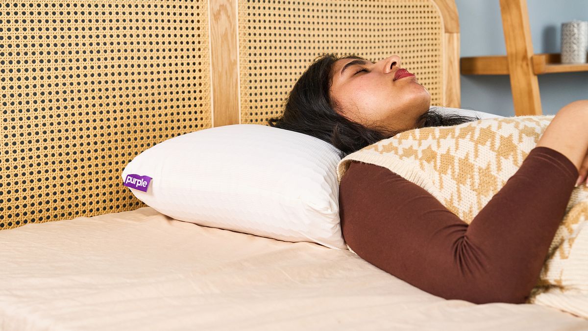 Woman sleeping on a white pillow with a purple tag on a bed with a rattan headboard