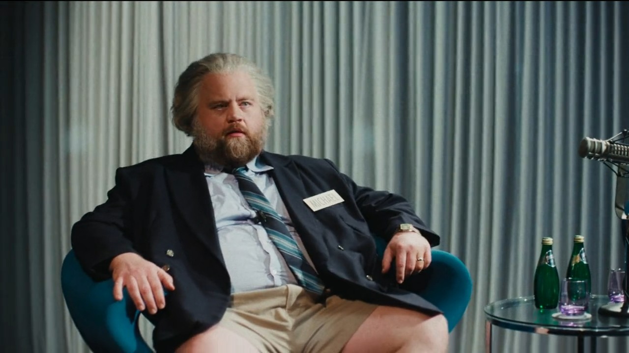 Paul Walter Hauser siting in a chair with shorts on in The Luckiest Man in America.