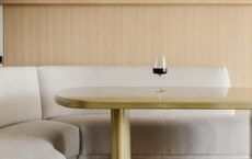 A dining table with curving sofa and a single wine glass kept atop