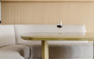 A dining table with curving sofa and a single wine glass kept atop