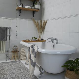 White bathroom with a white bathtub, a patterned floor rug and plant-like accessories