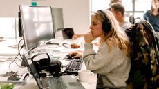 Young female software developer coding in Java programming language while sitting at a desk in an open plan office space.