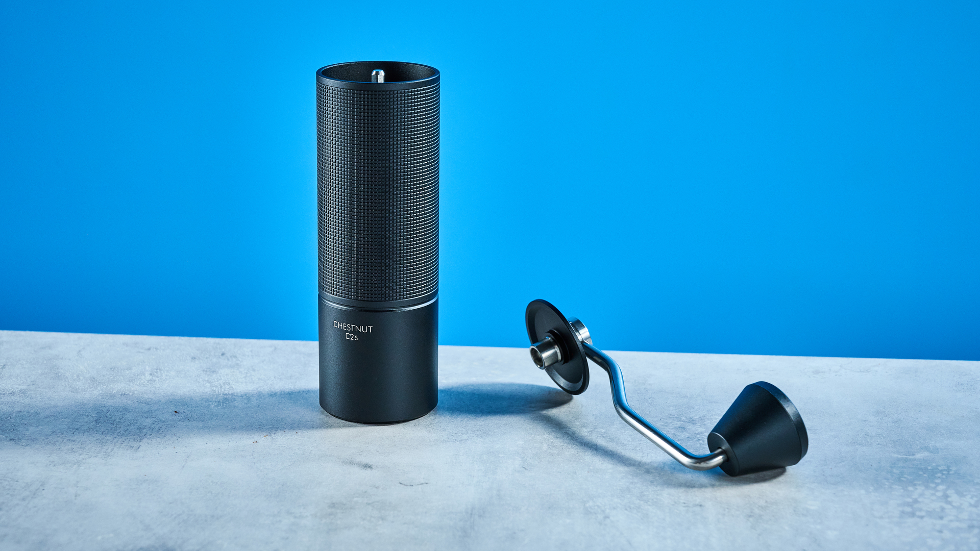 the timemore chestnut c2s coffee grinder in black showing its hand crank and catch chamber photographed against the blue tom's guide background