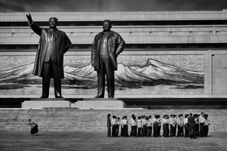 Group of people dwarfed by giant statues of North Korean leaders