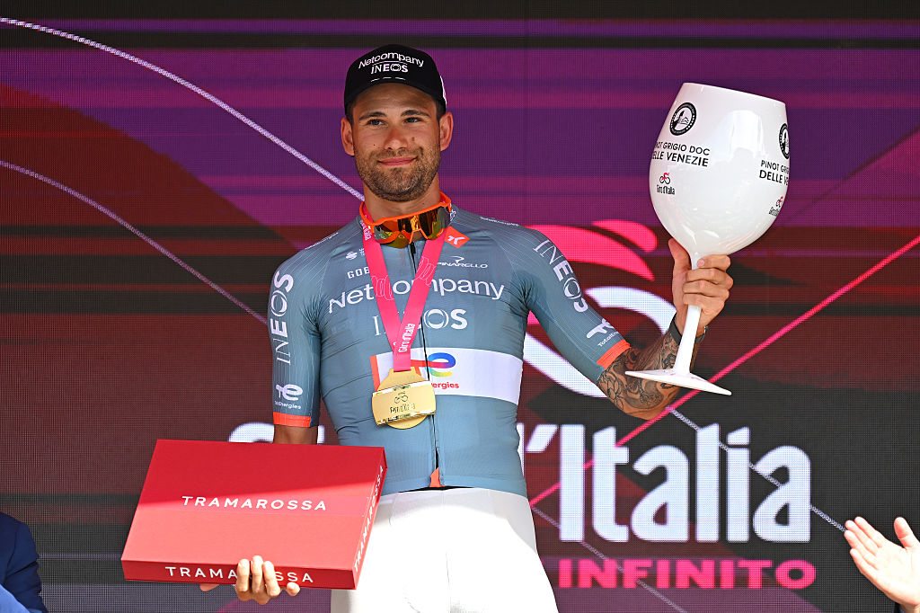 Ganna holds a huge glass and box on the podium, prizes for winning stage 10