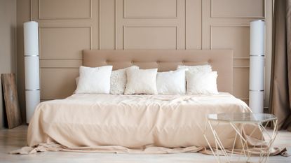 A mattress on a bed covered in beige bedding and white throw pillows.