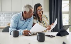 Couple look at pension documents as they organise inheritance tax plan while sitting at kitchen table.