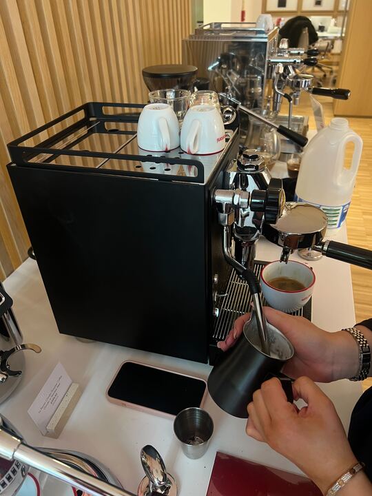 Image of two hands steaming milk on a black La Pavoni Mini Cellini Semi-Professional Domestic Coffee Machine on a white countertop.