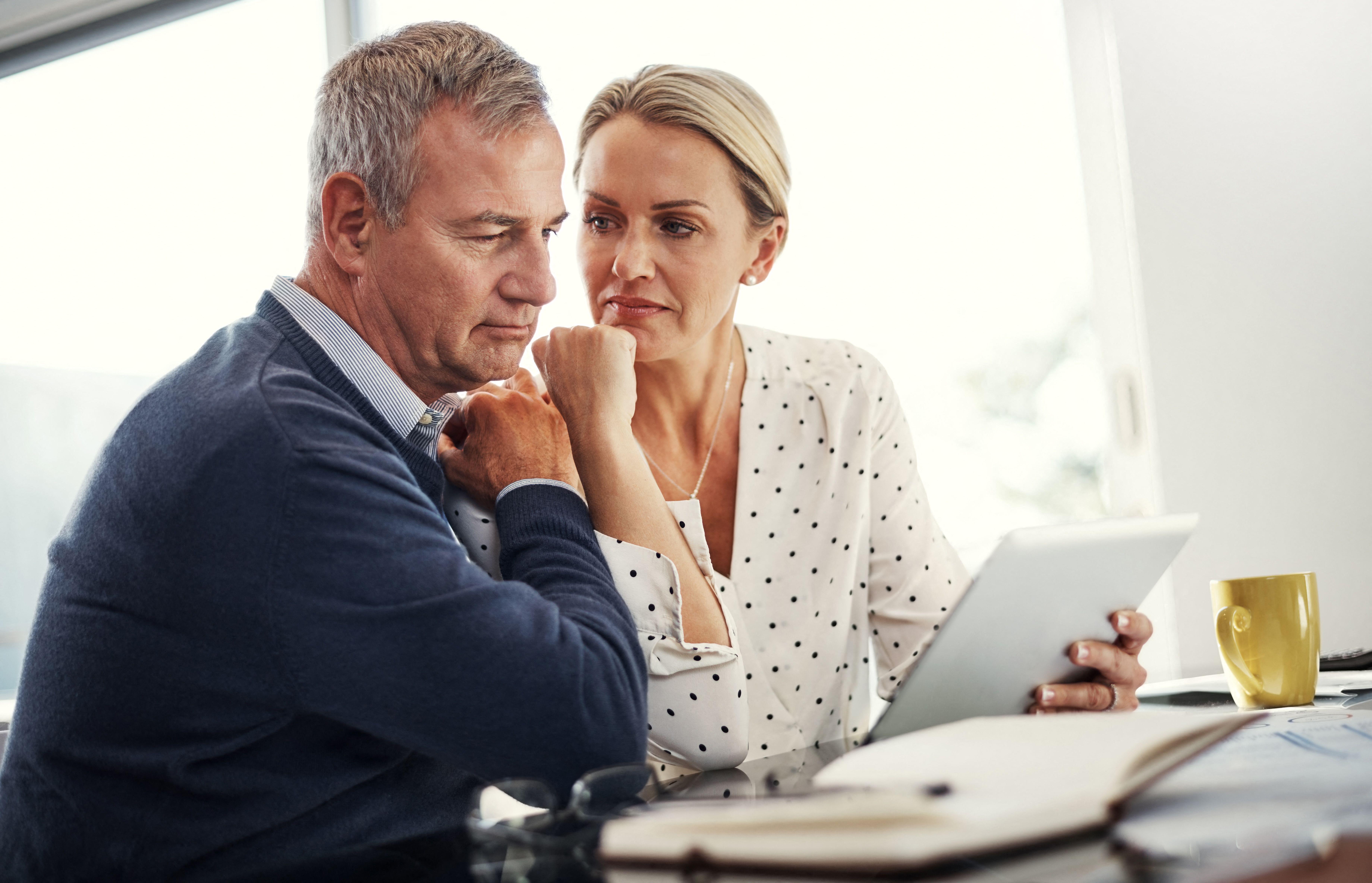 2R5HP65 Saving is priority. a mature couple using a digital tablet while going through paperwork at home.