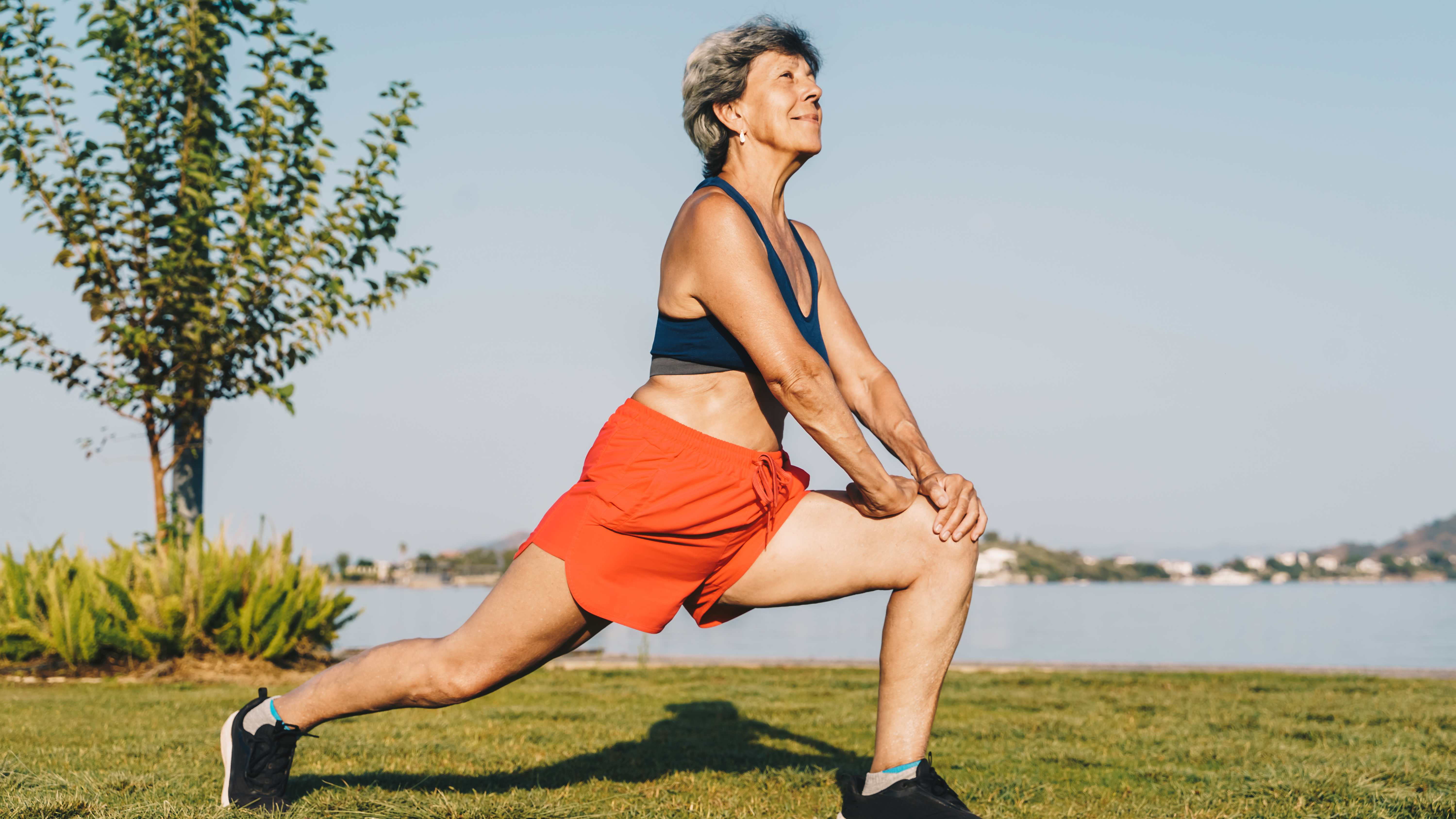 A woman performs a low lunge outside on a stretch of grass. 