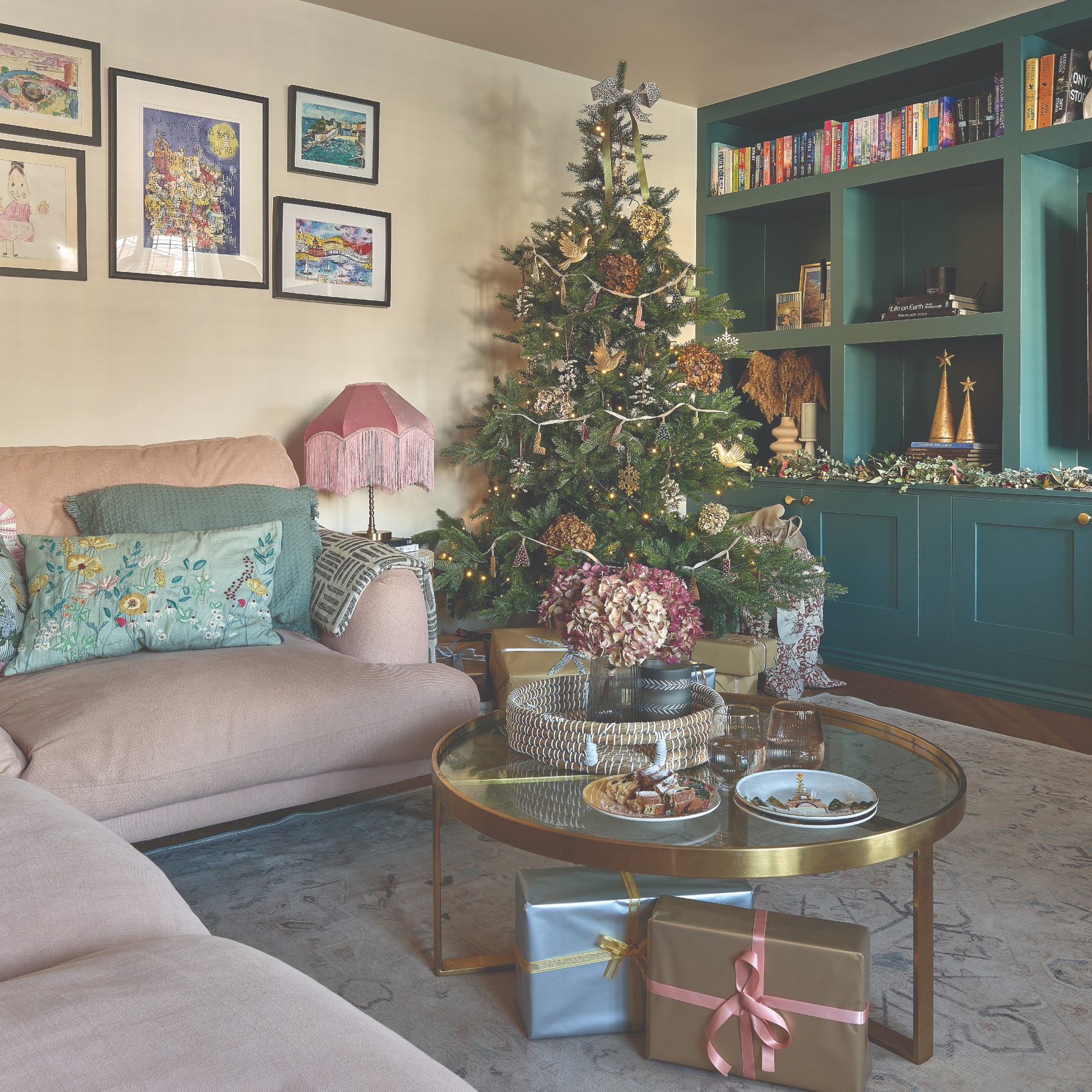 A living room with a pink corner sofa and a round glass coffee table with a decorated Christmas tree in the corner