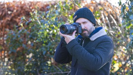 Professional photographer Dan Mold photographed outdoors with his eye to a Sony A7R IV camera that has a Sony FE 100mm f2.8 Macro G Master OSS lens attached to it
