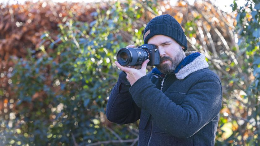 Professional photographer Dan Mold photographed outdoors with his eye to a Sony A7R IV camera that has a Sony FE 100mm f2.8 Macro G Master OSS lens attached to it