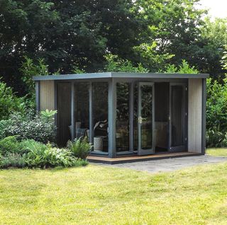 a wood ang black door panel garden room by John Lewis in a corner of a lush garden full of plants and hedges