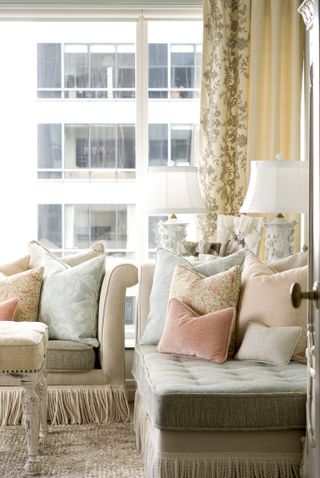 apartment living room with couch and chaise, fringing on bottom edge of couches, pink and blue cushions, coffee table