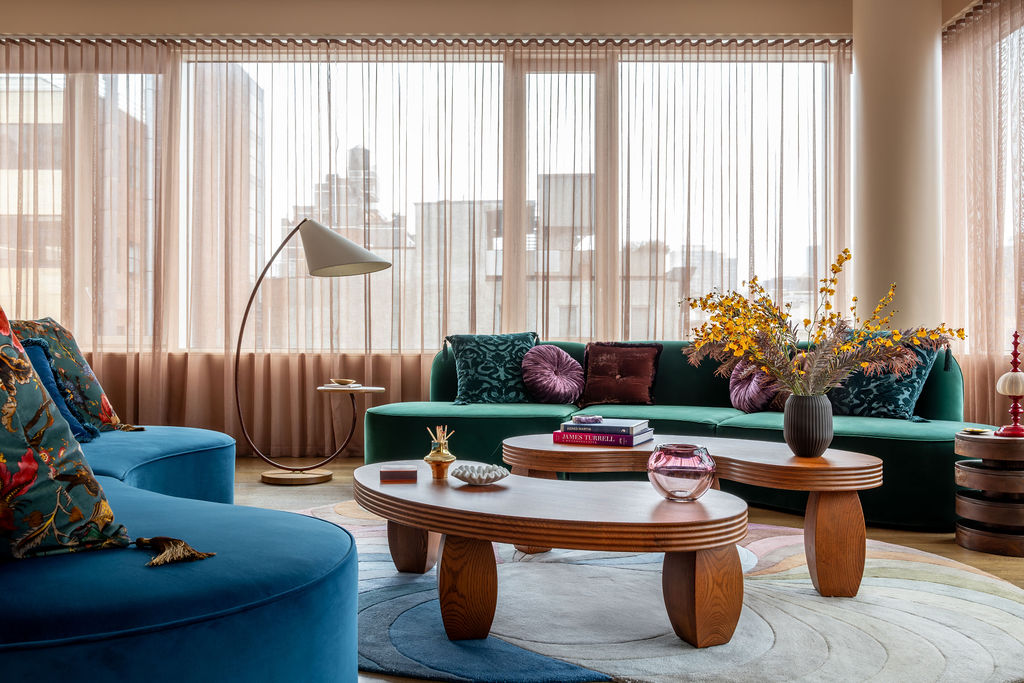 A city apartment filled with a jewel-toned blue and green sofas, plus patterned accent pillows and a whimsical coffee table.