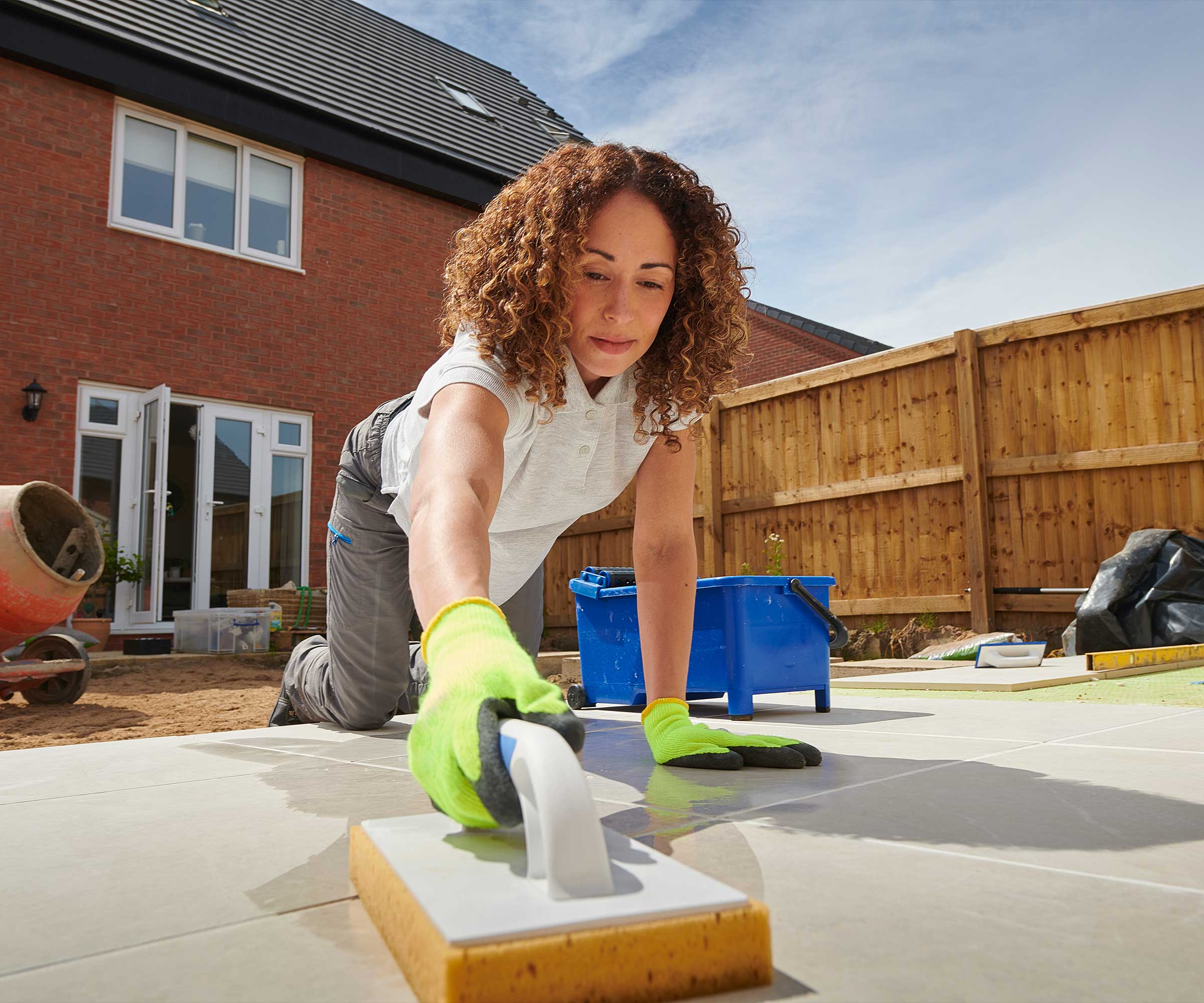 woman on her hands and knees grouting paving slabs in a residential garden