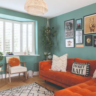 A green-painted living room with a burnt orange velvet corner sofa and a raffia pendant on the overhead lighting