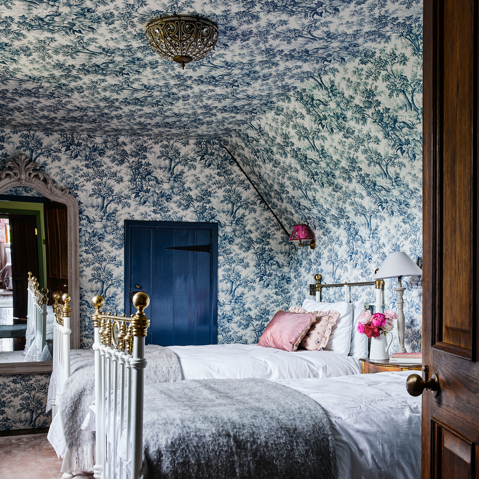 attic bedroom with blue toile wallpaper over walls and ceiling and twin wrought iron beds