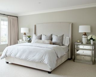 A netural bedroom with pale blue striped sheets and mirrored bedside table