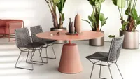 A round pink concrete outdoor table with black rope chairs