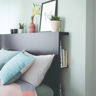 A mint-painted bedroom with a black storage headboard concealing books