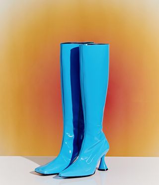 Ladies knee high boots in patent turquoise blue, white floor, orange and red glow background