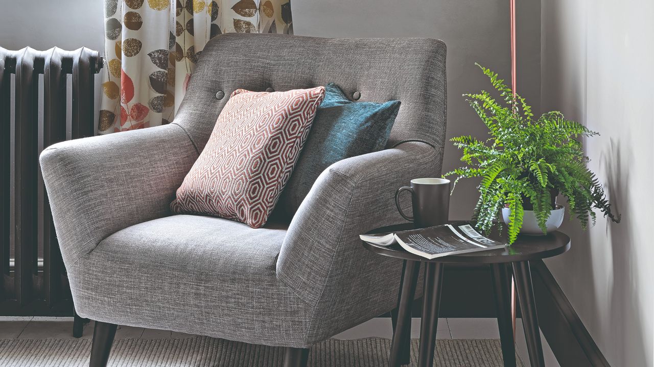 A reading corner with a grey chair, a side table with a book and a mug