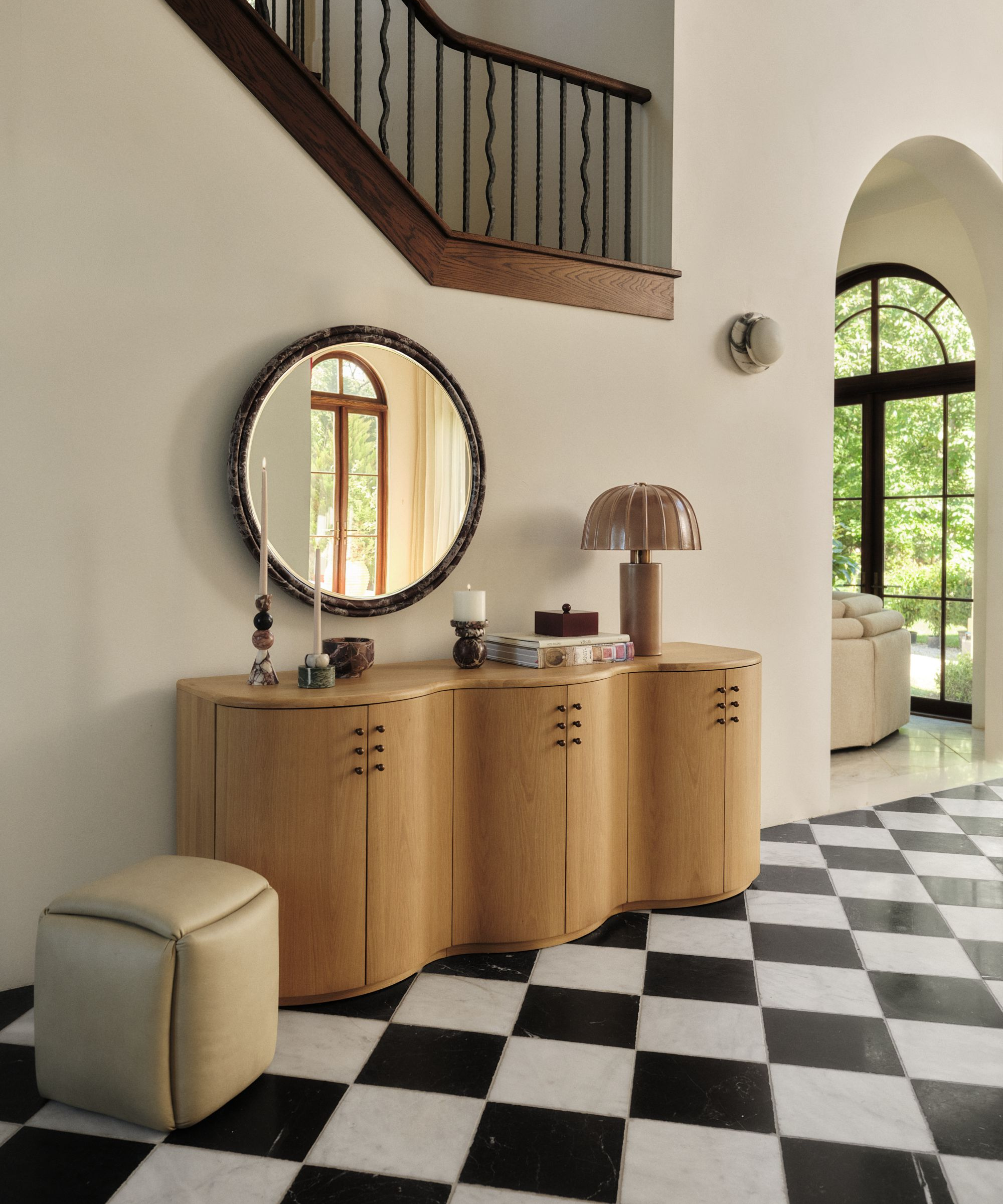 an entryway credenza with candles, a lamp, books, and a mirror above