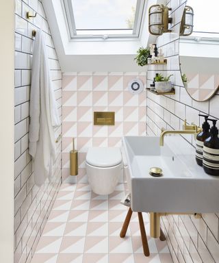 An example of small bathroom flooring ideas showing pink and white geometric floor and wall tiles with a white sink and gold hardware