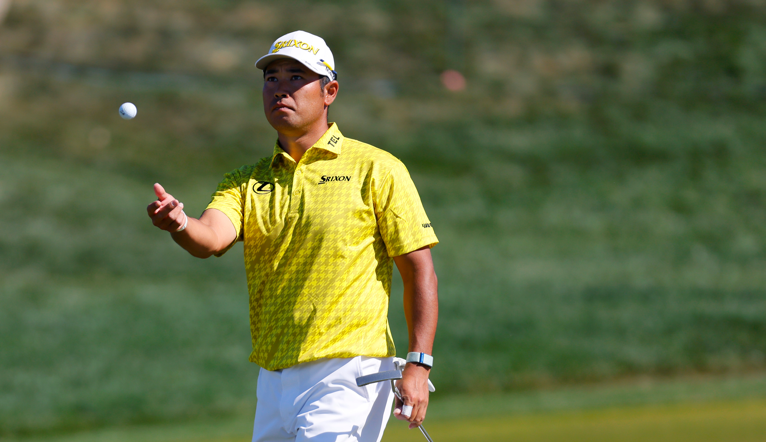 Hideki Matsuyama throws a ball to his caddie